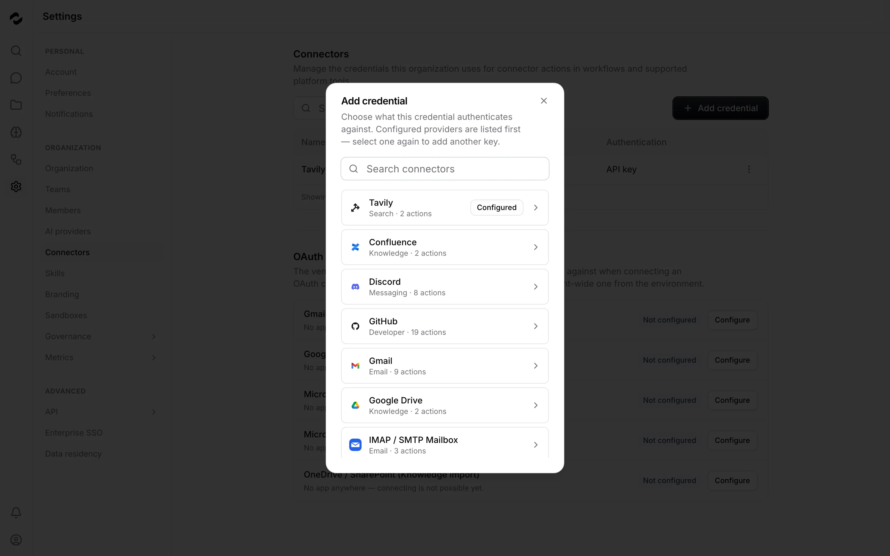 The Add credential dialog over the Settings > Connectors table, listing the shipped connectors as cards with their category tags and action counts, a search field at the top, and the already-configured Tavily connector at the head of the list.